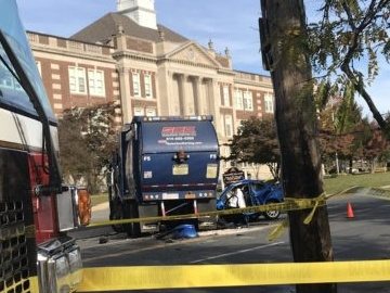 Police tape around a garbage truck and a crushed car on Boston Post Road in daylight.