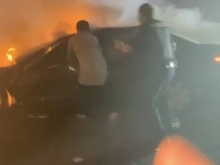 People trying to reach a burning car on Boston Post Road at night.