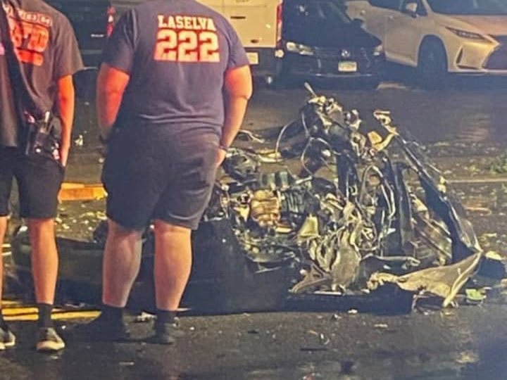 Firefighters standing beside the wreckage of a vehicle on Boston Post Road at night.
