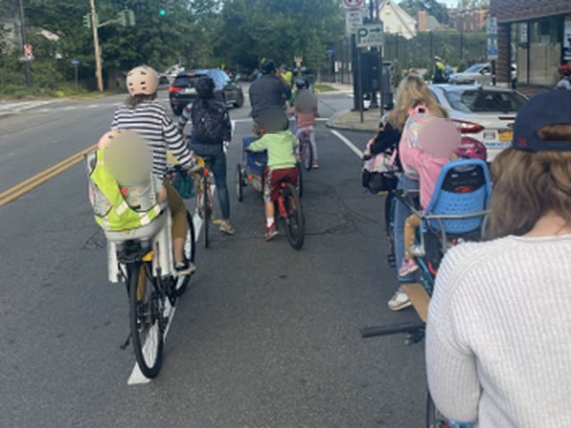 Parents and children riding bikes to school together down a street.