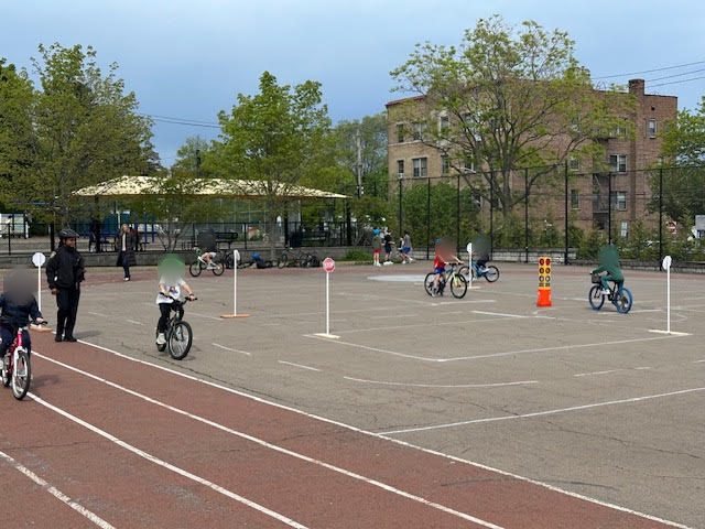 Children riding bikes through a cone course on a school blacktop.