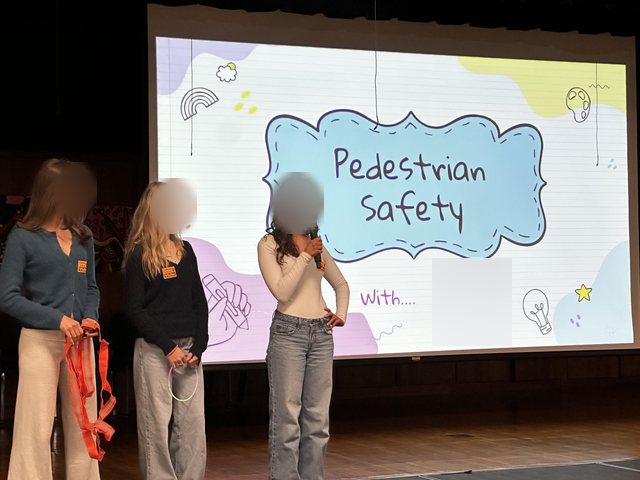 Three students presenting a pedestrian safety talk in a school auditorium.